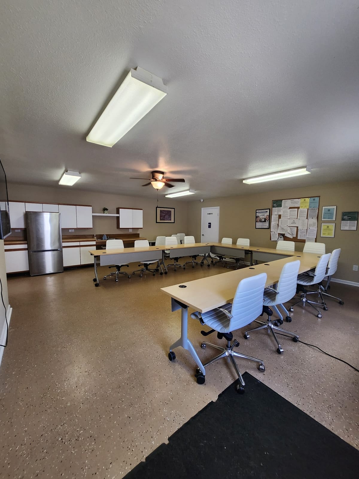 The community room at Prince Frederick Senior, with maple conference tables, white cushioned rolling chairs, a kitchenette, and a ceiling fan