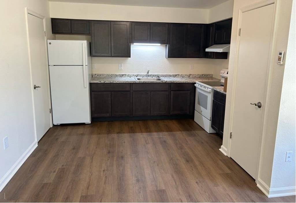 A renovated kitchen at Prince Frederick Senior with dark shaker cabinets, a white refrigerator and electric range, granite-look countertops, and wood-look plank flooring