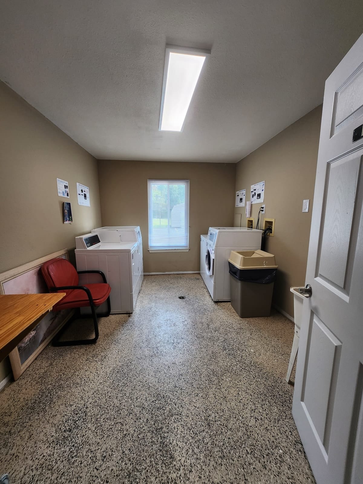 The on-site laundry room at Prince Frederick Senior, with white top-loading washers and dryers, a window, a folding table, and a chair